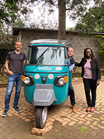 Three people standing by motorbike taxi