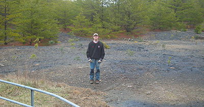 Man standing outside in front of a group of pine trees